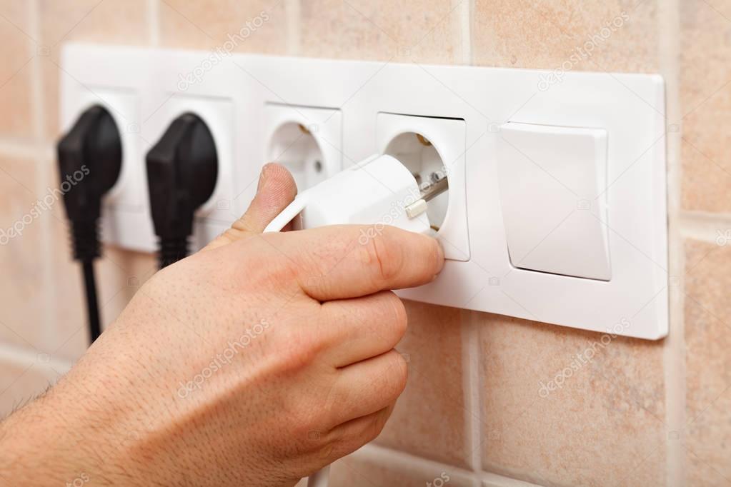 Hand plugging a power cord into electrical wall fixture