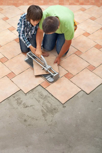 Kleiner Junge lernt, wie man eine keramische Bodenfliese schneidet — Stockfoto
