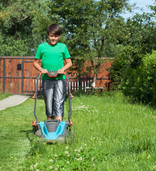 Ung pojke klippa gräset med en gräsklippare — Stockfoto