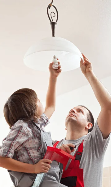 Boy helping father mounting a ceiling lamp - screwing in the lig — Stock Photo, Image