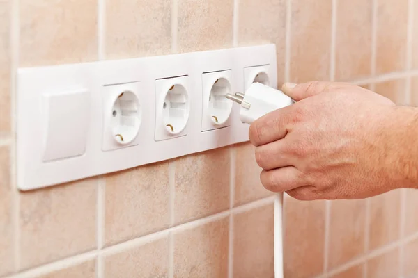 Męskiej ręki podłączyć przewód zasilający do gniazdka elektrycznego w ścianie — Zdjęcie stockowe
