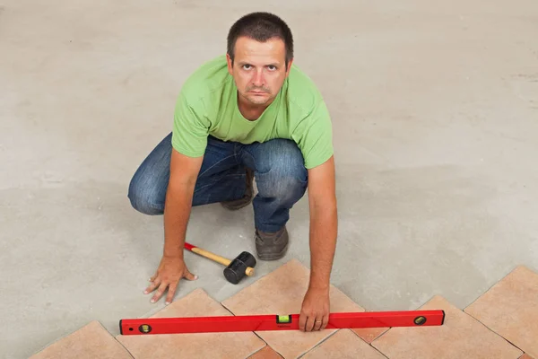 Mann verlegt keramische Bodenfliesen - Überprüfung mit Ebene, Draufsicht — Stockfoto