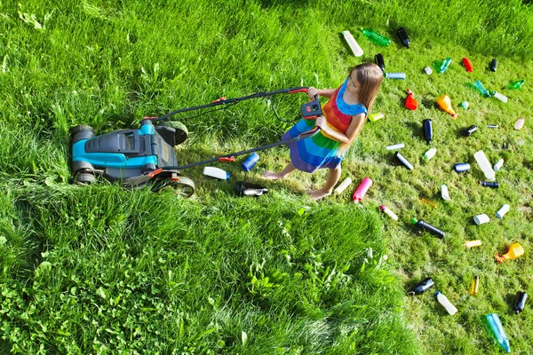 Young girl pushing a lawnmower and leaving plastic litter behind — Stock Photo, Image