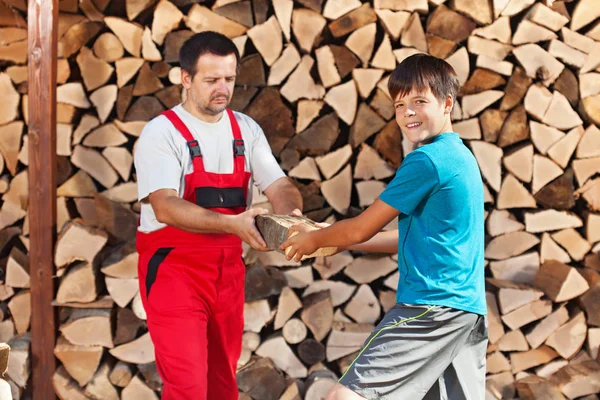 Teenage boy helping father stack the firewood — Stock Photo, Image