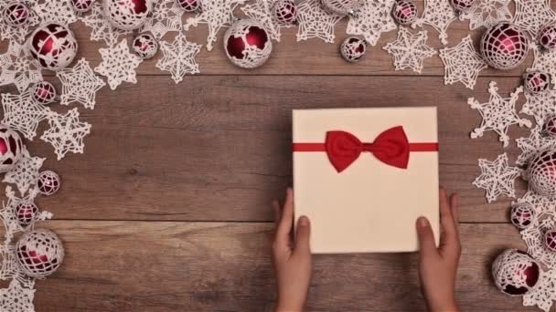 木製のテーブル上の季節のフレーム内部の Fir とクリスマス プレゼントを開く手のトップ ビュー — ストック動画