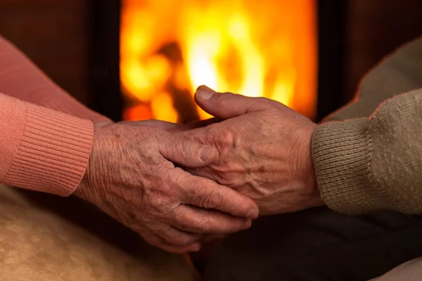 Senior old hands comforting each other in front of fireplace — Stock Photo, Image