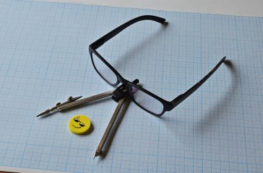 Çizim kağıdı üzerine bir pusula, gözlük ve sarı silgi..