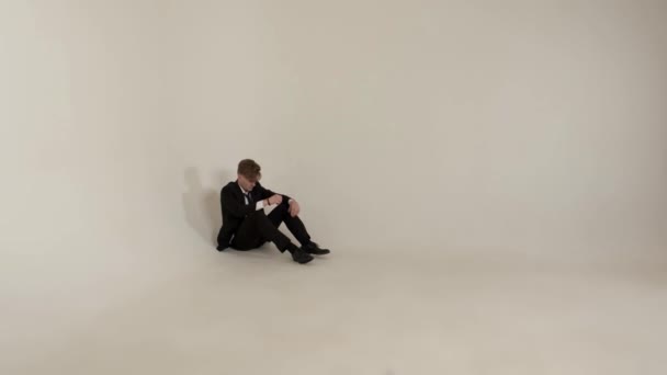 Ο τύπος που κάθεται σε άδειο δωμάτιο στο λευκό φόντο. Έννοια της μοναξιάς. — Αρχείο Βίντεο