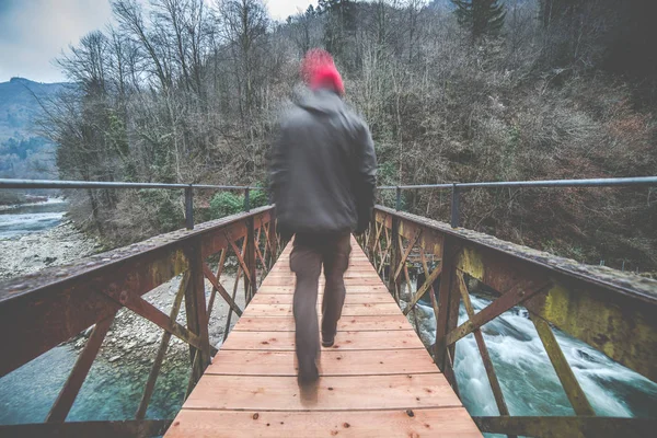 L'uomo attraversa un ponte pedonale in ferro e legno sul fiume — Foto Stock