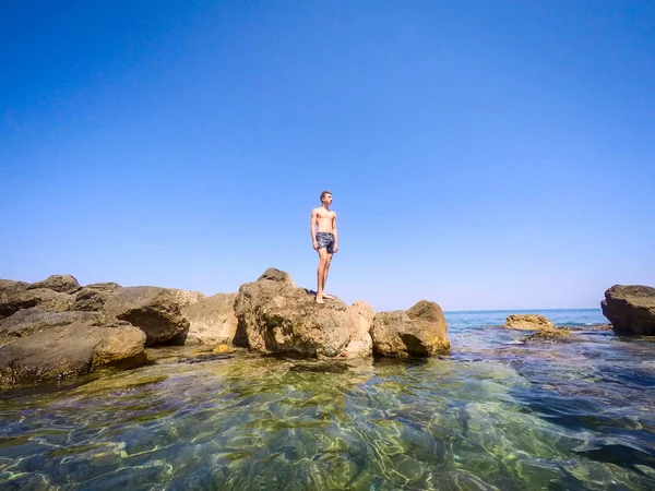 Tonåringen stående på klipporna vid havet - sommartid — Stockfoto