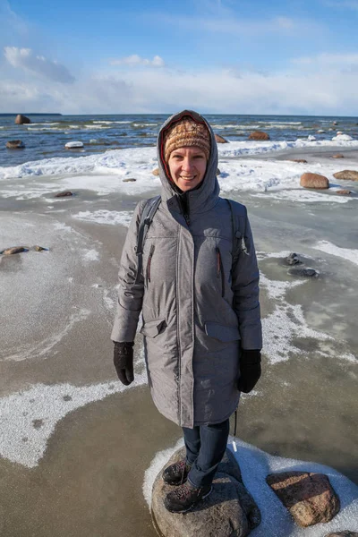 寒くて晴れた日石の上に滞在の若い笑顔の女性。バルト海の海岸 — ストック写真