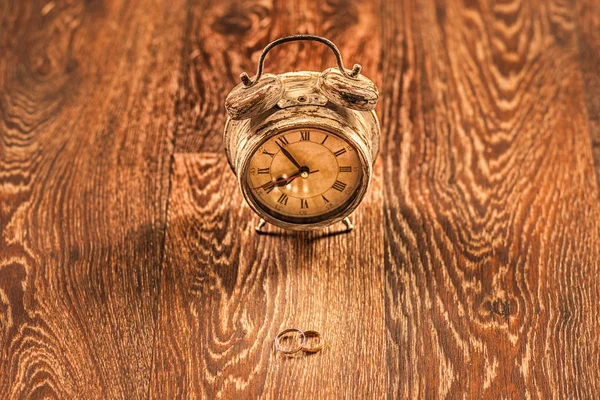 Retro alarm clock on wooden table with wedding rings — Stock Photo, Image