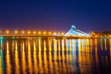 Parlak Daugava Nehri Köprüsü ve gece yansımalar. Letonya Riga'da modern Milli Kütüphane