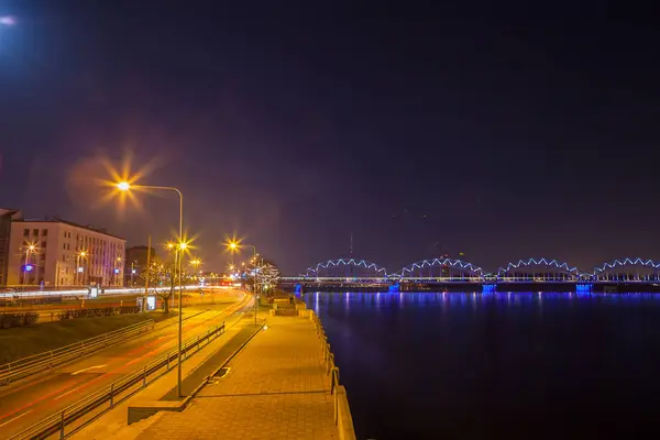 Embankment road and Illuminated railway bridge at night in Riga, Letónia — Fotografia de Stock