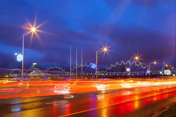 Estrada iluminada ao longo do rio Daugava e ponte ferroviária à noite em Riga, Letónia — Fotografia de Stock