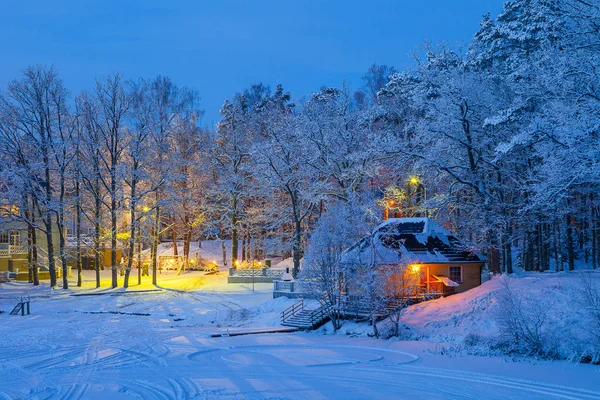 Escena nevada de invierno de cabañas iluminadas en previsión cerca del lago congelado —  Fotos de Stock