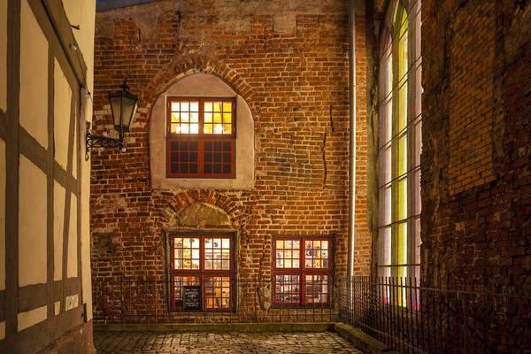 RIGA, LATVIA - 25 DEC 2015. Red brick wall of old house in Riga, way to most romantic cafe in old town. Night scene, illuminated windows. Stock Image