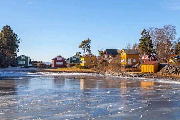 Ξύλινες καμπίνες χρώμα του νησιού με παγωμένη θάλασσα στο προσκήνιο. Σκανδιναβικό στιλ. Ηλιόλουστη χειμωνιάτικη ημέρα — Φωτογραφία Αρχείου