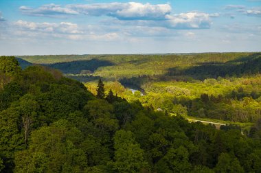 Güzel gökyüzü ve bulutlar yeşil orman, Güneş tarafından kaplı tepeler üzerinde. Gauja Nehri, Letonya.