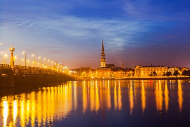Büyük taş köprü ve St. Peter Kilisesi ile eski Riga gece manzarası. Işıklı şehir güneş battıktan sonra. Daugava Nehri üzerinden panoramik görünüm