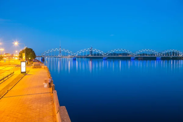 Daugava aterro e a ponte ferroviária sobre o rio. Cena panorâmica noturna em Riga, Letônia — Fotografia de Stock