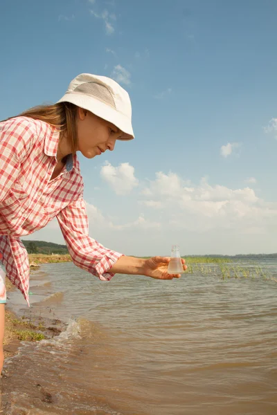 Prueba de pureza del agua. Mujer sosteniendo frasco químico con agua, lago o río en el fondo . — Foto de Stock