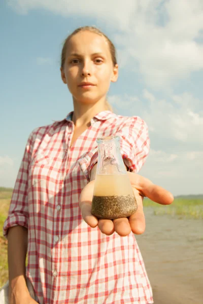 Teste de pureza de água. Mulher segurando frasco químico com água, lago ou rio no fundo . — Fotografia de Stock