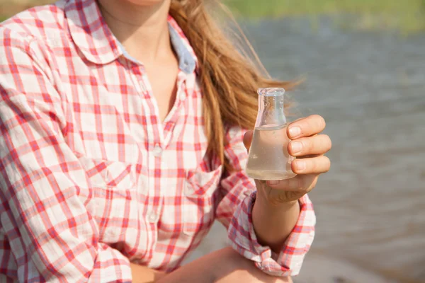 Su saflık testi su, göl veya nehir içinde belgili tanımlık geçmiş ile kimyasal bir şişesi tutan el. — Stok fotoğraf