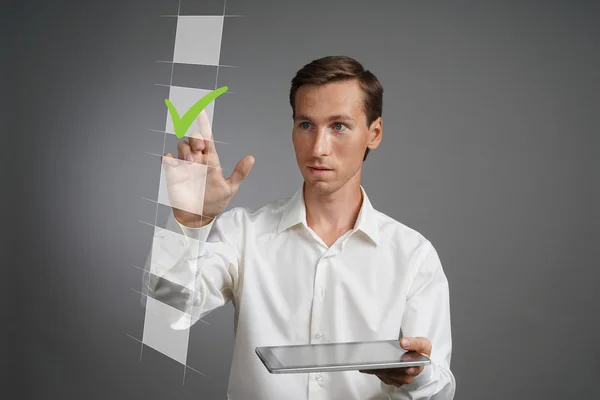 Junger Geschäftsmann in weißem Hemd mit Tablet-Computer, der eine Checkliste ankreuzt. grauer Hintergrund. — Stockfoto