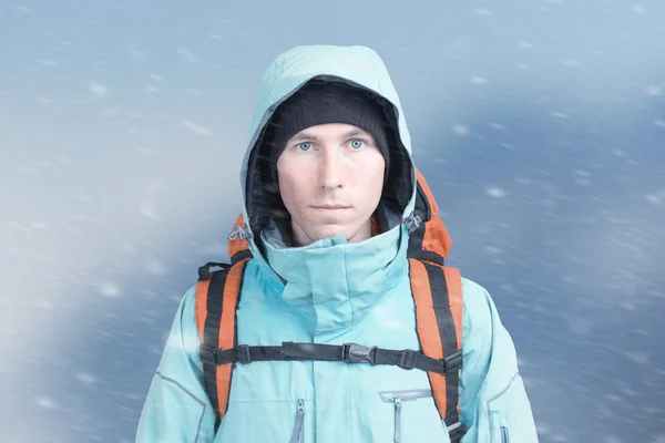 Horolezec muž stojí v sněhové bouři, horské krajiny v pozadí. — Stock fotografie