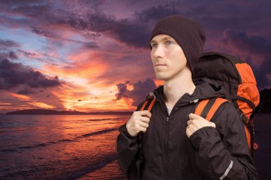 Deniz günbatımı arka plan üzerinde sırt çantası ile genç adam.