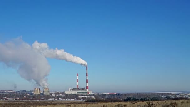 Central térmica o una fábrica con chimeneas humeantes en el horizonte. Humo contaminante en el cielo azul claro . — Vídeo de stock