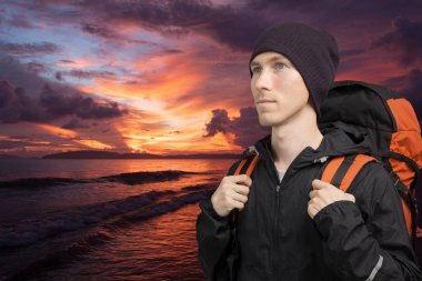 Deniz günbatımı arka plan üzerinde sırt çantası ile genç adam.