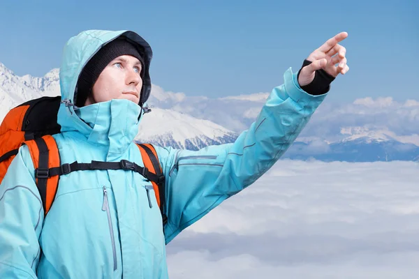 De bergbeklimmer wijzend op piek, staande tegen een berg winterlandschap. — Stockfoto