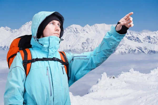 L'alpiniste pointant vers le sommet, debout contre un paysage de montagne d'hiver . — Photo
