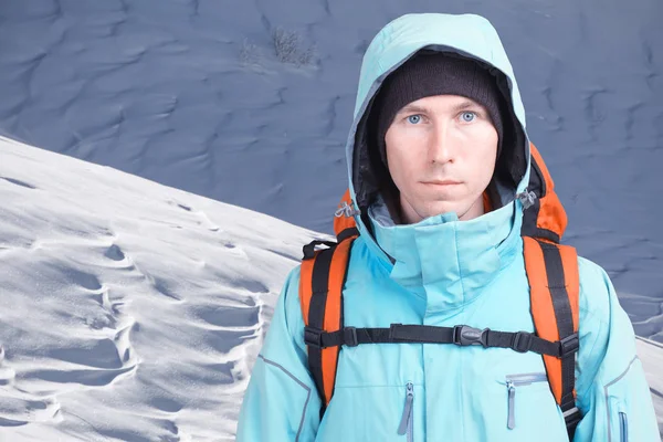 Homem alpinista com uma mochila em um fundo de paisagem de montanha. Olhando para a câmera . — Fotografia de Stock