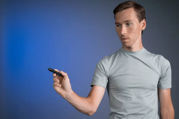 Man in grijs t-shirt trekt iets op transparante scherm, op blauwe achtergrond — Stockfoto