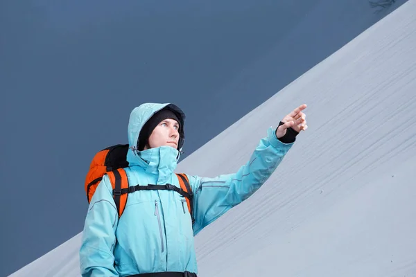 Der Bergsteiger zeigt auf den Berghang und steht vor einer winterlichen Berglandschaft. — Stockfoto