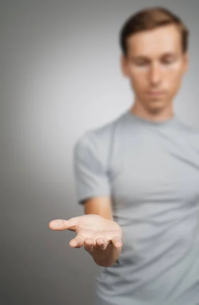 Hombre sosteniendo algo en blanco en su mano sobre un fondo gris . — Foto de Stock