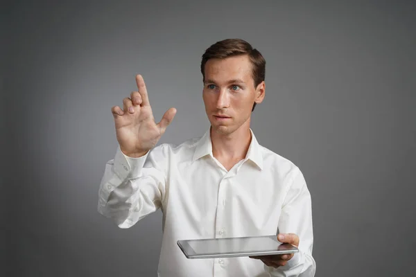 Jeune homme travaillant avec écran virtuel sur fond gris, tenant une tablette . — Photo