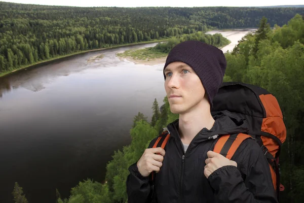 Młody człowiek z plecakiem stoi naprzeciwko rzeki. — Zdjęcie stockowe