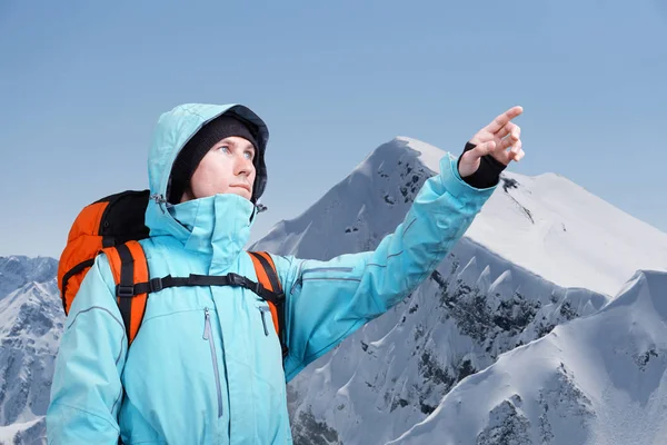 Der Bergsteiger zeigt auf den Gipfel und steht vor einer winterlichen Berglandschaft. — Stockfoto