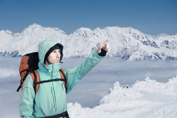 Альпинист указывает на вершину, стоя против зимнего горного пейзажа . — стоковое фото