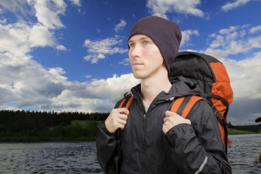 Bir sırt çantası ile genç adam bir nehir önünde duruyor.