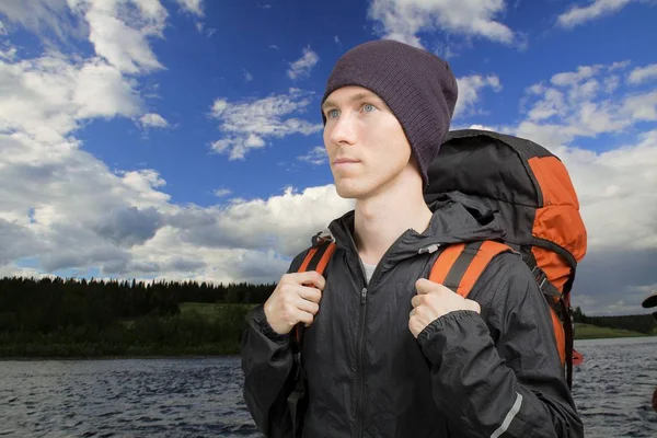 Bir sırt çantası ile genç adam bir nehir önünde duruyor.