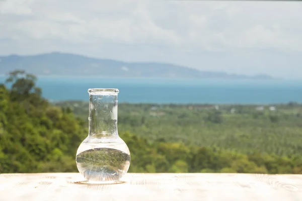 Sauberes Wasser in einem gläsernen Laborkolben auf einem Holztisch auf Meeresgrund. ökologisches Konzept, Schutz der Wasserressourcen, Prüfung der Reinheit und Qualität des Wassers. — Stockfoto