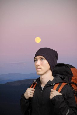 Sırt çantasında Dağları olan genç adam. Moon ile tepelik gece manzarası.