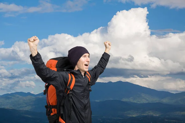 Junger Mann mit Rucksack steht mit erhobenen Händen auf einem Berg. — Stockfoto