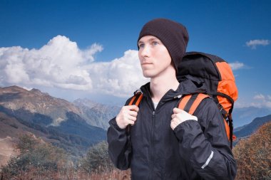 Bir dağ manzarası arka plan üzerinde sırt çantası ile genç adam ve beyaz bulutlar mavi bir gökyüzü portresi. Hiking, tırmanma dağ.
