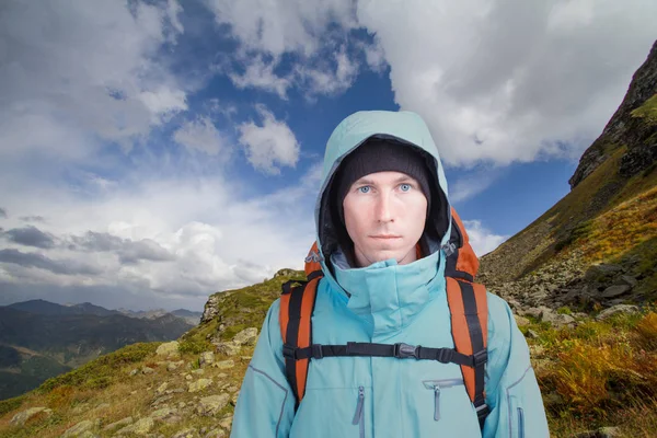 Bir dağ manzarası arka plan üzerinde sırt çantası ile genç adam ve beyaz bulutlar mavi bir gökyüzü portresi. Hiking, tırmanma dağ.